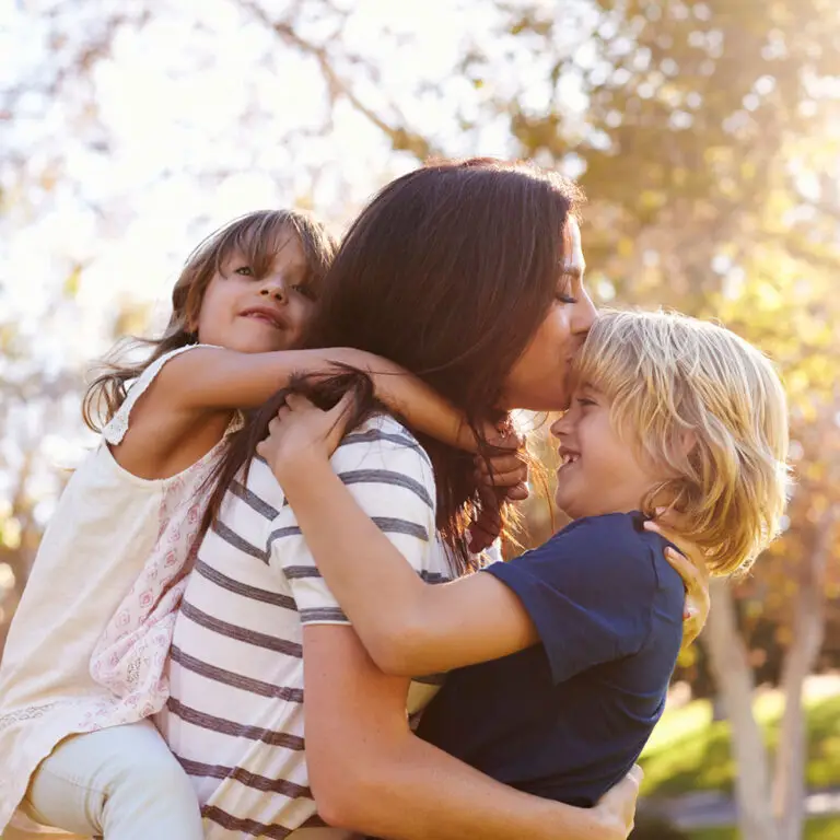 Mother carrying son and daughter as they play in park.